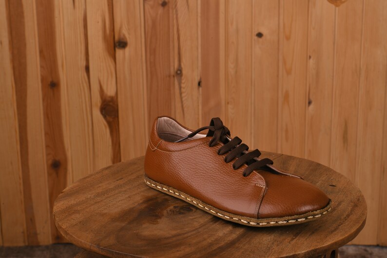 May include: A brown leather lace-up shoe with a stitched sole. The shoe is sitting on a wooden surface.