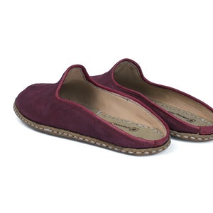 May include: A pair of burgundy leather slippers with a stitched edge and a brown sole.