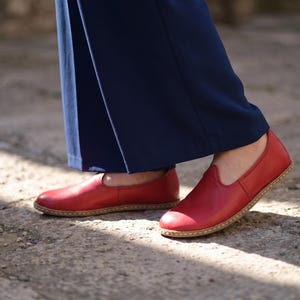 Puede incluir: Un par de zapatos rojos de cuero sin cordones con punta redondeada y suela marr&oacute;n claro. Los zapatos se usan con pantalones azul marino. Los zapatos son de cuero.