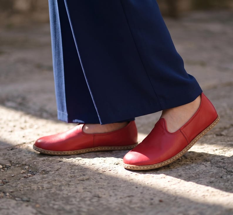 Puede incluir: Un par de zapatos rojos de cuero sin cordones con punta redondeada y suela marr&oacute;n claro. Los zapatos se usan con pantalones azul marino. Los zapatos son de cuero.