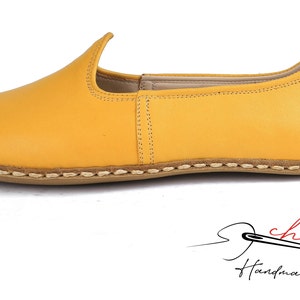 May include: A pair of yellow leather slip-on shoes with a stitched edge and a brown sole.