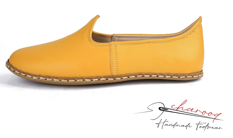 May include: A pair of yellow leather slip-on shoes with a stitched edge and a brown sole.