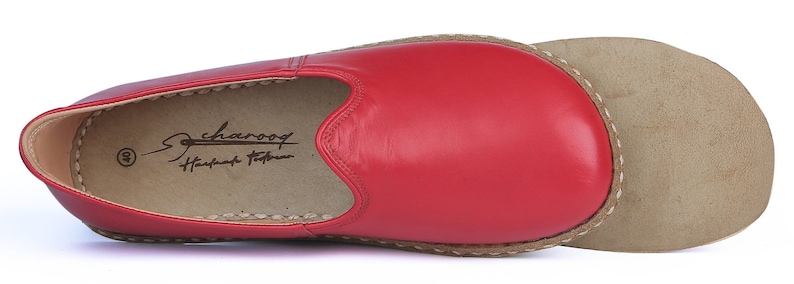 Puede incluir: Una zapatilla de cuero rojo con punta redondeada y suela separada de color beige. La zapatilla tiene el texto "Scharoof Handmade Footwear" impreso en el interior. La suela est&aacute; cosida a la parte superior del zapato con hilo blanco.
