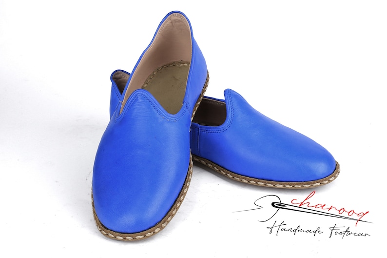 Pu&ograve; includere: Un paio di pantofole in pelle blu con un bordo cucito marrone. Le pantofole sono fatte a mano e hanno una punta a punta.