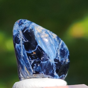 K&ouml;nnte beinhalten: Ein blauer und wei&szlig;er Tigerauge-Edelstein mit einer glatten, polierten Oberfl&auml;che. Der Stein hat ein einzigartiges, wirbelndes Muster und ist eine beliebte Wahl f&uuml;r Schmuck und Kristallheilung.