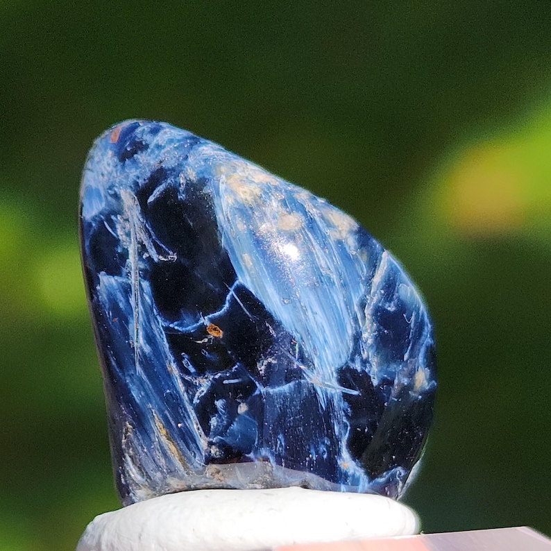 K&ouml;nnte beinhalten: Ein blauer und wei&szlig;er Tigerauge-Edelstein mit einer glatten, polierten Oberfl&auml;che. Der Stein hat ein einzigartiges, wirbelndes Muster und ist eine beliebte Wahl f&uuml;r Schmuck und Kristallheilung.