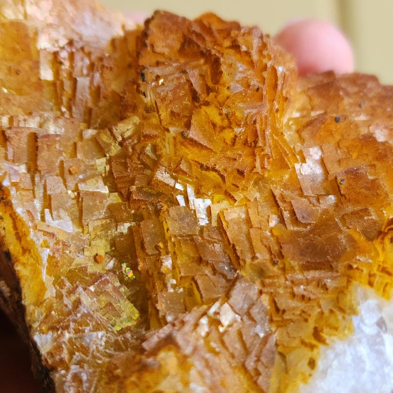 May include: Close-up of a mineral specimen with a crystalline structure. The mineral displays a warm, golden-yellow hue with a complex, layered appearance. The texture is rough and uneven, with a mix of sharp and rounded edges.