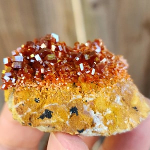 Op de afbeelding: Een cluster van oranje en rode vanadinietkristallen op een bruine matrix. De kristallen zijn scherp en goed gedefinieerd, met een metaalachtige glans.