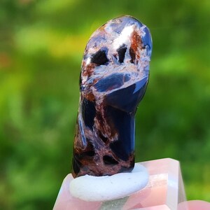 May include: A dark blue and brown gemstone with a unique swirling pattern. The gemstone is polished and has a smooth surface.