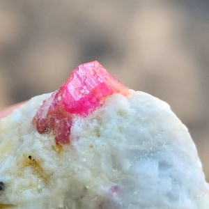 以下が含まれることがあります： 白とベージュの鉱物ベースの上に、鮮やかなピンク色の結晶が形成されています。 結晶は鋭く角張った構造をしており、光を反射します。 鉱物はざらざらとした質感で、印象的なコントラストを生み出しています。