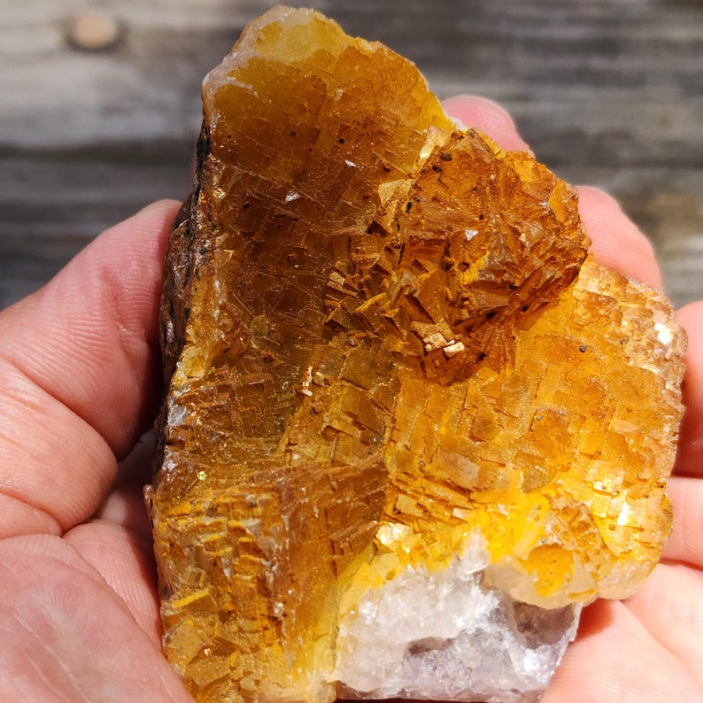 May include: A rough, golden-yellow mineral specimen with a crystalline structure. The stone has a layered appearance with a mix of warm, earthy tones. A small, lighter-colored section is visible at the base of the specimen.