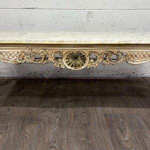 May include: A rectangular coffee table featuring a light-colored marble top and a cream-painted wooden frame. The apron displays intricate carved scrollwork, lattice patterns, and a central medallion. It stands on four curved cabriole legs.
