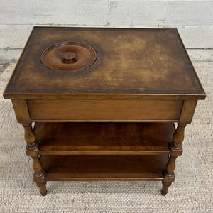 May include: A wooden side table with a leather top and a round inset. The table has two shelves and turned legs.