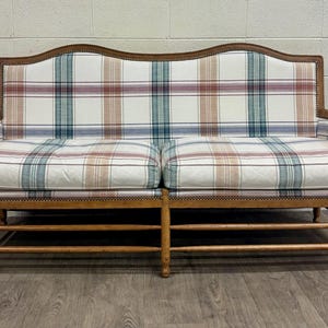 May include: A two-seater sofa with a plaid pattern in shades of red, blue, and tan on a white background. The wooden frame has a curved top and armrests. The sofa is supported by a wooden base.