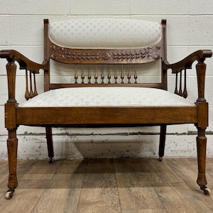 May include: A wooden antique settee with a white fabric cushion and carved details. The settee has a spindle back and turned legs.