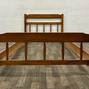 May include: A wooden bed frame with a simple design. The frame is made of solid wood and has a natural finish. The headboard and footboard are both rectangular and have a slightly curved top edge. The frame has a slatted base for support.