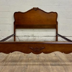 May include: A wooden bed frame with a curved headboard and footboard. The frame is a warm brown color with ornate carvings on the footboard. The legs are curved and the headboard has a decorative top.