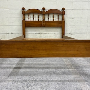 May include: A wooden bed frame with a headboard and footboard. The frame is made of solid wood and has a natural finish. The headboard has a simple design with turned posts and a slatted back.