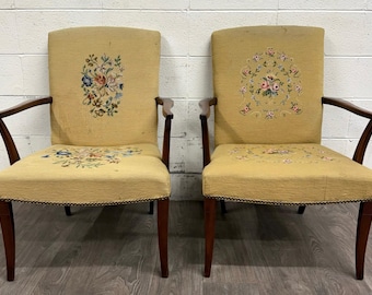 May include: A pair of armchairs featuring mustard yellow fabric upholstery with intricate floral embroidery on the backrests and seats. The chairs have dark brown wooden frames, angled armrests, and straight legs with decorative metal nailhead trim.