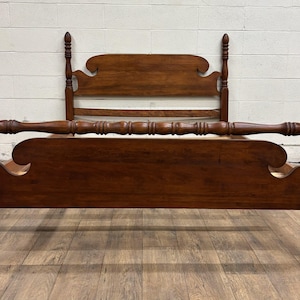 May include: A dark brown wooden bed frame with a headboard and footboard. The headboard has a decorative top with a curved design. The bed frame has four tall, turned posts and a horizontal rail.