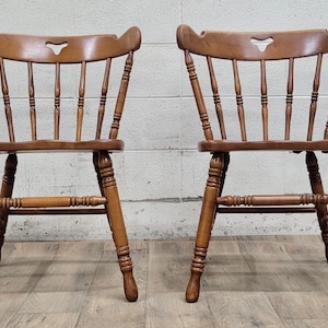 May include: Two wooden chairs with a simple design. The chairs have a slatted back and seat, and a curved top rail with a cutout in the shape of a heart. The chairs are made of a light brown wood.