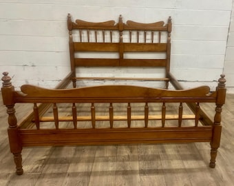 May include: A wooden bed frame with a warm, honey-toned finish. The headboard features a decorative top with vertical slats, while the footboard has a curved design. The frame includes turned posts and horizontal rails, creating a classic, vintage aesthetic.
