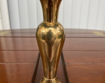 May include: A small, polished brass vase with a flared top and a rounded body. The vase is sitting on a wooden surface.
