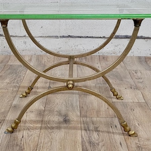 May include: A gold metal table with a glass top. The table has a curved design with a circular base.