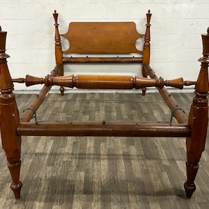 May include: A wooden bed frame with a headboard and footboard. The frame is made of dark wood and has a simple design. The headboard is rectangular and has a slightly curved top. The footboard is also rectangular and has a slightly curved top. The frame is supported by four legs.