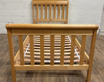 May include: A light-colored wooden bed frame with a headboard and footboard. The frame has a slatted base and a curved headboard design. The bed frame is made of light-colored wood and has a simple, classic design.