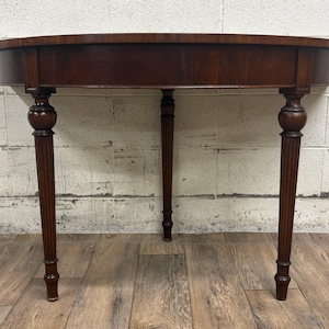 May include: A dark brown wooden console table with an oval top and three legs. The table has a simple, elegant design.