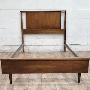 May include: A wooden bed frame with a headboard and footboard. The frame is made of dark wood and has a simple, mid-century modern design.