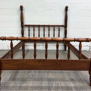 May include: A brown wooden bed frame featuring four tall posts topped with spherical finials. The headboard and footboard are constructed with horizontal rails and vertical spindles, showcasing a natural wood grain finish throughout the structure.
