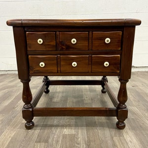 May include: A dark brown wooden end table with eight drawers and a square base. The drawers have white ceramic knobs.
