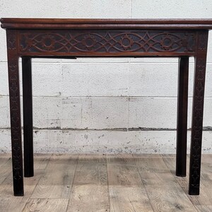 May include: A dark brown wooden table with a carved design on the top and legs. The table has a rectangular top and four legs.