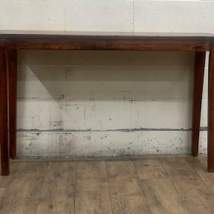 May include: A rectangular wooden table with a dark brown finish. The table has four slender legs and a simple, elegant design. The table is approximately 48 inches long, 16 inches wide, and 30 inches tall.