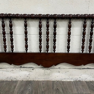 May include: A dark brown wooden headboard featuring a series of vertical, spindle-style turned posts along the top rail. The base of the headboard consists of a solid horizontal wooden panel with a scalloped, curved bottom edge design.