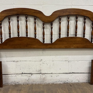 May include: A wooden headboard with a warm brown finish. The headboard features a curved top with a series of vertical spindles and decorative finials. The design is traditional, suitable for a bed frame. The headboard is approximately 60 inches wide.