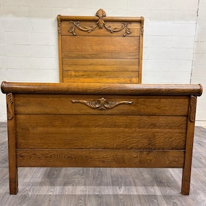 May include: An antique wooden bed frame with a headboard and footboard. The headboard features carved floral details and a decorative top. The bed frame is made of light brown wood and has a classic design.
