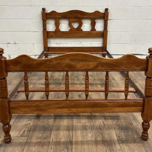 May include: A wooden bed frame with a headboard featuring a heart-shaped cutout. The frame is made of stained wood with turned posts and spindles. The bed frame is approximately 78 inches long and 60 inches wide.