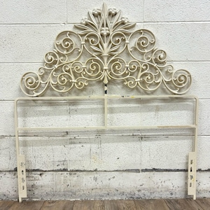 May include: White metal headboard with a decorative scrollwork design. The headboard has a floral motif at the top and is attached to a metal frame.
