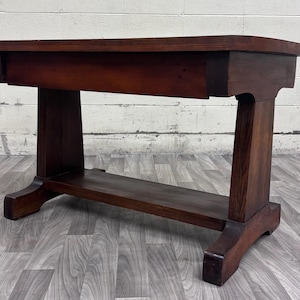 May include: A dark brown wooden console table featuring a rectangular top, a wide apron, and two sturdy vertical supports connected by a horizontal base shelf. The table is constructed with visible wood grain and a smooth, polished finish.