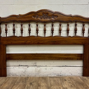 May include: A vintage wooden headboard with a dark brown finish. The headboard features a decorative floral carving at the top and a series of turned spindles. The design includes horizontal support beams and vertical posts, showcasing a classic style.