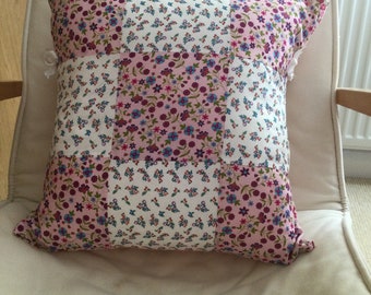 May include: A patchwork pillow with a white background and pink, purple, and blue floral patterns.