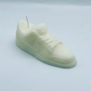 Può includere: Una candela bianca a forma di scarpa da ginnastica con uno stoppino che sporge dalla parte superiore.