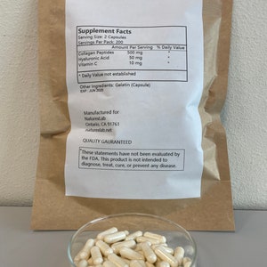 May include: A brown paper bag with a white label containing supplement facts for a product with 500 mg of collagen peptides, 50 mg of hyaluronic acid, and 10 mg of vitamin C. The label also states that the product is manufactured for NaturexLab in Ontario, CA 91761. A clear glass dish filled with white capsules is in the foreground.