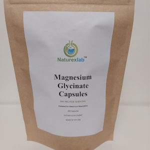 May include: A brown paper bag with a white label that reads "Naturexlab™ Magnesium Glycinate Capsules 500 MG PER SERVING Chelated for Maximum Absorption 250 Capsules DIETARY SUPPLEMENT MADE IN THE USA". A pile of white capsules are in front of the bag.