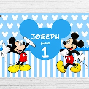 May include: A blue and white banner featuring Mickey Mouse characters. The banner reads "Joseph turns 1" with a large blue Mickey Mouse ear in the background.