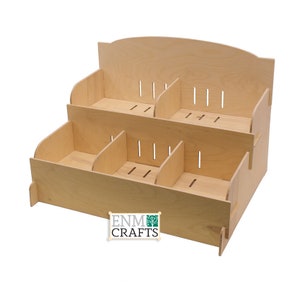 May include: A three-tiered wooden display stand with multiple compartments. The stand is made of light wood and has a natural finish. The stand is perfect for displaying small items, such as jewelry, crafts, or other collectibles. The stand is labeled "ENM CRAFTS".