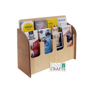 Peut inclure: Un porte-brochures en bois avec cinq fentes pour des brochures. Le porte-brochures est en bois clair avec une teinte brun foncé. Le porte-brochures a un devant incurvé et un dos plat. Le porte-brochures est étiqueté "ENM CRAFTS".